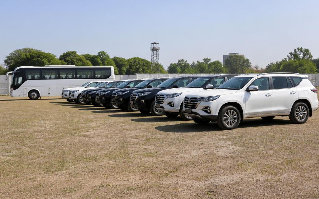 Row of white and black SUVs parked beside a coaster bus for a convoy